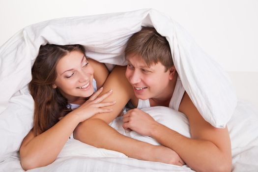 Beautiful young couple relaxing in bed at home over white