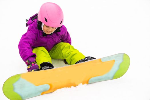 Snowboard Winter Sport. little girl learning to snowboard, wearing warm winter clothes. Winter background.