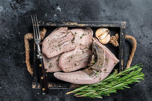 Cooked Boiled veal or beef tongue sliced in a wooden tray. Black background. Top view.