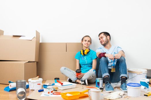 Happy couple together sitting on floor among cardboard boxes. Young man and woman relaxing after moving in their new house. House remodeling and interior renovation. Families moving concept.