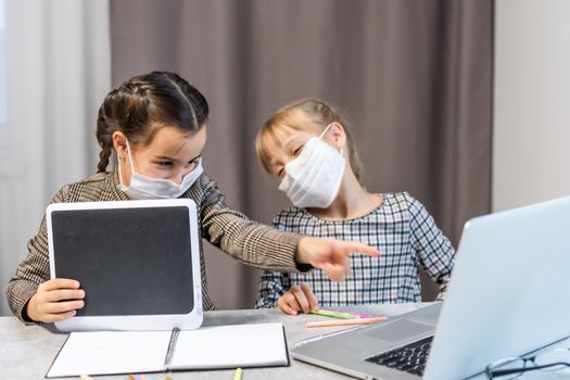 Distance Learning. School Girls At Laptop Wearing Mask Studying Online Sitting at the table at home