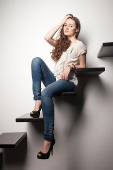 Portrait of beautiful stylish brunette with long hair looking at camera while sitting on steps