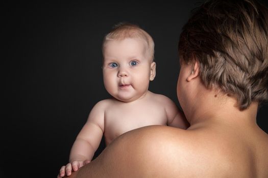 Cute baby looking over fathers shoulder at the camera, isolated on black