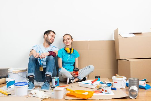 Happy couple together sitting on floor among cardboard boxes. Young man and woman relaxing after moving in their new house. House remodeling and interior renovation. Families moving concept.