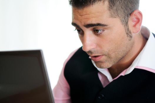 A successful businessman with glasses wearing vest and pink shirt looking at a little computer