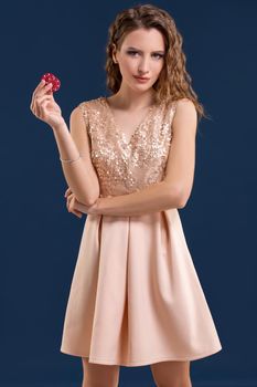 Beautiful young woman in dress with casino chips in the hands on dark blue background. Casino. Emotions. Gambling