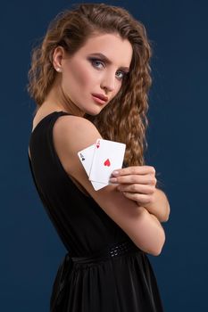 Beautiful woman in black dress holding two aces as a sign for poker game on dark blue background, gambling and casino