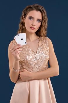Young beautiful woman playing in casino. Woman in light dress holding the winning combination of poker cards on dark blue background. Two aces