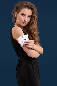 Beautiful woman in black dress holding two aces as a sign for poker game on dark blue background, gambling and casino