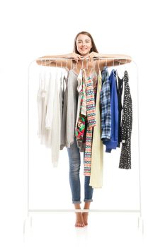 Barefoot smiling brunette tiptoes behind hanger with clothes.Studio shot