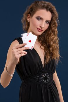 Beautiful woman in black dress holding two aces as a sign for poker game on dark blue background, gambling and casino