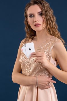 Young beautiful woman playing in casino. Woman in light dress holding the winning combination of poker cards on dark blue background. Two aces