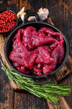 Fresh raw diced slices of red beef fiilet meat in cast iron pan. Dark wooden background. Top view.