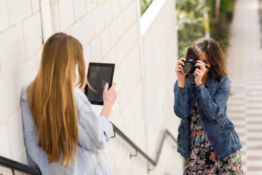 Two young tourist women taking photographs with digital tablet and analogic reflex camera. Travelers concept.