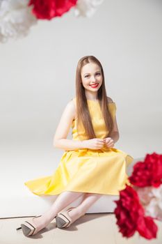 Portrait of beautiful smiling model sitting on floor in yellow dress.Studio shot.