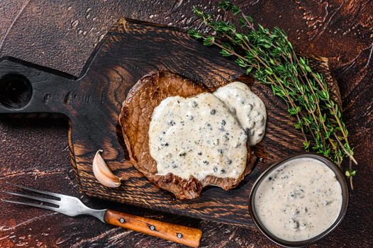 Grilled sirloin beef meat steak with peppercorn sauce. Dark background. Top view.