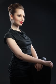 Portrait of beautiful woman in black dress with hairstyle and red lips looking at camera