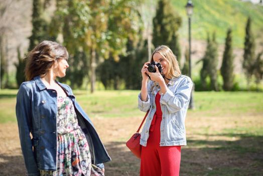 Two young tourist women taking photographs with analogic reflex camera in urban park. Travelers concept.