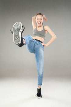 Portrait of young cheerful woman with open mouth looking at camera while raising her right leg