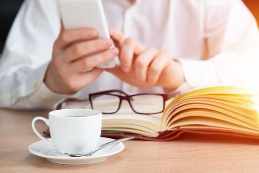 Man in white shirt using smartphone as sit at desk with cup of coffee. Business application and mobile technology. Internet internet browsing and communication. Coffee break at workplace in office