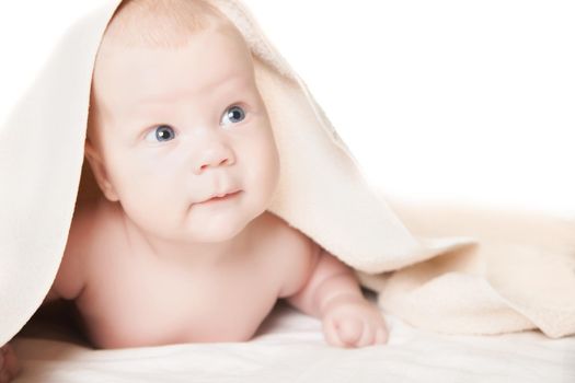 Cute baby under the towel after bathing lies smiling and looking aside on white background