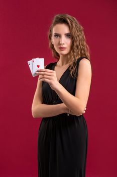 Young woman in black dress holding playing cards against a red background. Studio shot. Poker. Casino