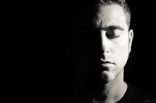 Portrait of a man with half face on shadow. Eyes closed.