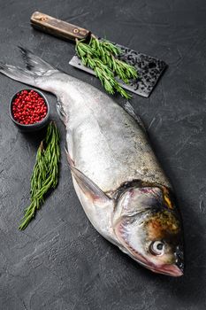 Raw whole fish silver carp with pink pepper and rosemary. Black background. Top view.