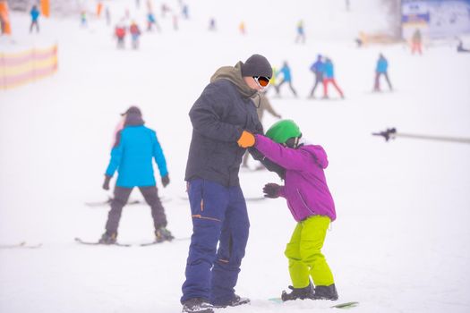 Instructors teach a child on a snow slope to snowboard