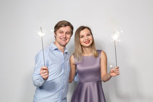 Party, celebration, event and holidays concept - man dressed in blue shirt and woman dressed in purple dress hold a firework stick.