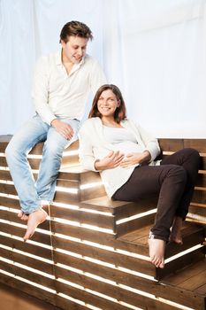 Couple at home sitting on stairs. Pregnant woman