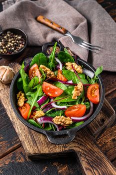 Healthy bistro green salad with mix leaves mangold, swiss chard, spinach, arugula and nuts in a pan. Dark wooden background. Top view.