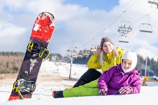 Mother and daughter with snowboards are playing in the snow