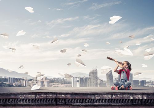 Cute kid girl sitting on house roof and looking in spyglass