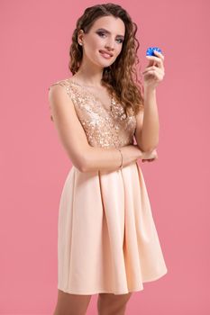 Beautiful young woman in dress with casino chips in the hands on pink background. Casino. Emotions. Gambling