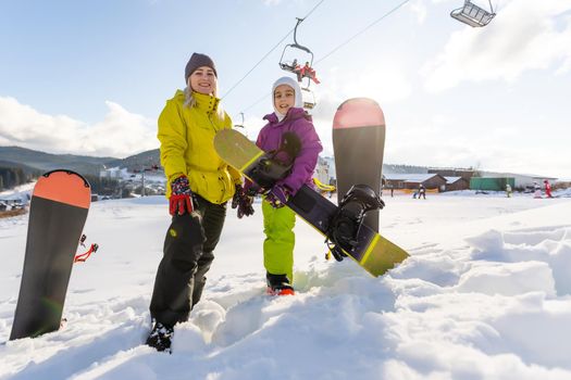 Mother and daughter with snowboards are playing in the snow