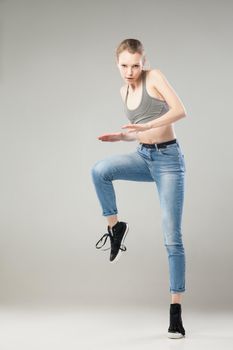 Portrait of young blonde woman looking at camera while standing tiptoe on left leg with raised right leg