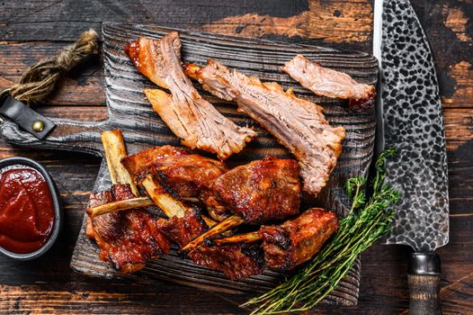 Barbecue grilled sliced veal short spare loin ribs on a cutting board. Dark wooden background. Top view.