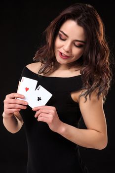 Young woman playing in the gambling on black background. Sexy brunette in a dress with two aces in her hand