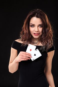 Young woman playing in the gambling on black background. Sexy brunette in a dress with two aces in her hand