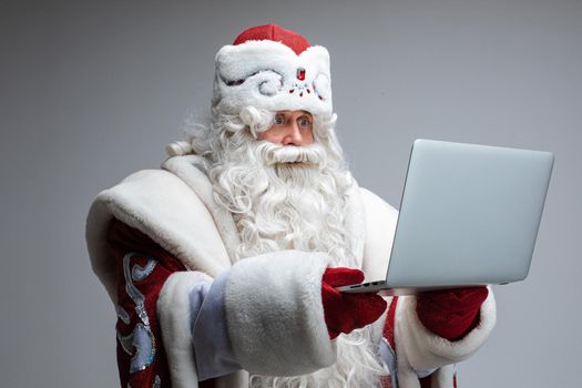 Stock photo of senior Father Frost in traditional costume looking at laptop with fear and wide open eyes.