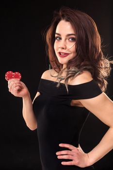 Smiling girl holding a gambling chips in her hands on black background. Sexy brunette in a dress. Poker.