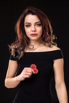 Smiling girl holding a gambling chips in her hands on black background. Sexy brunette in a dress. Poker.