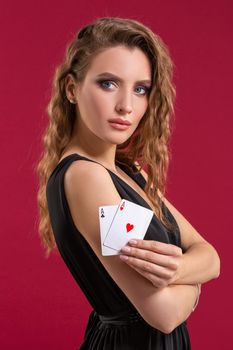 Beautiful young woman in black dress with a playing cards on red background. Casino. Poker