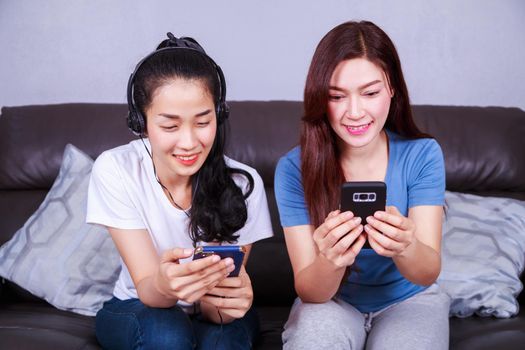 two young woman listening to music in headphones with moblie on sofa at home