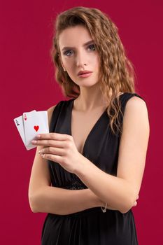 Beautiful young woman in black dress with a playing cards on red background. Casino. Poker