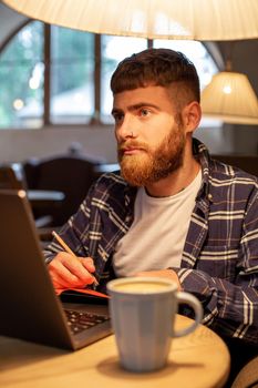 Casual business man or freelancer planning his work on notebook, working on laptop computer with smart phone, cup of coffee on table at coffee shop or home office, working from cafe concept