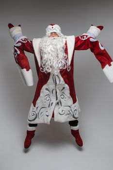Stock photo of full length Father Frost in traditional costume with long white beard standing in tree yoga pose with arms in namaste above his head.