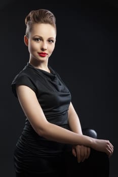 Portrait of beautiful woman in black dress with hairstyle and red lips looking at camera