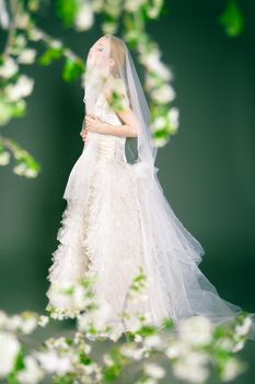 Beautiful young bride has veil over her head and face. Over blurred nature background.